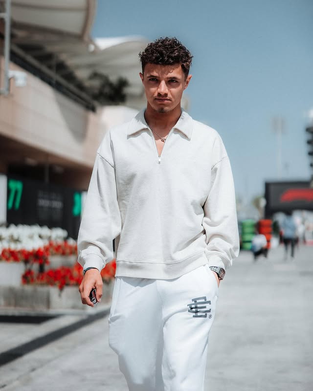 A full-length photo of Lando Norris walking outdoors, wearing a white long-sleeved shirt and white sweatpants.