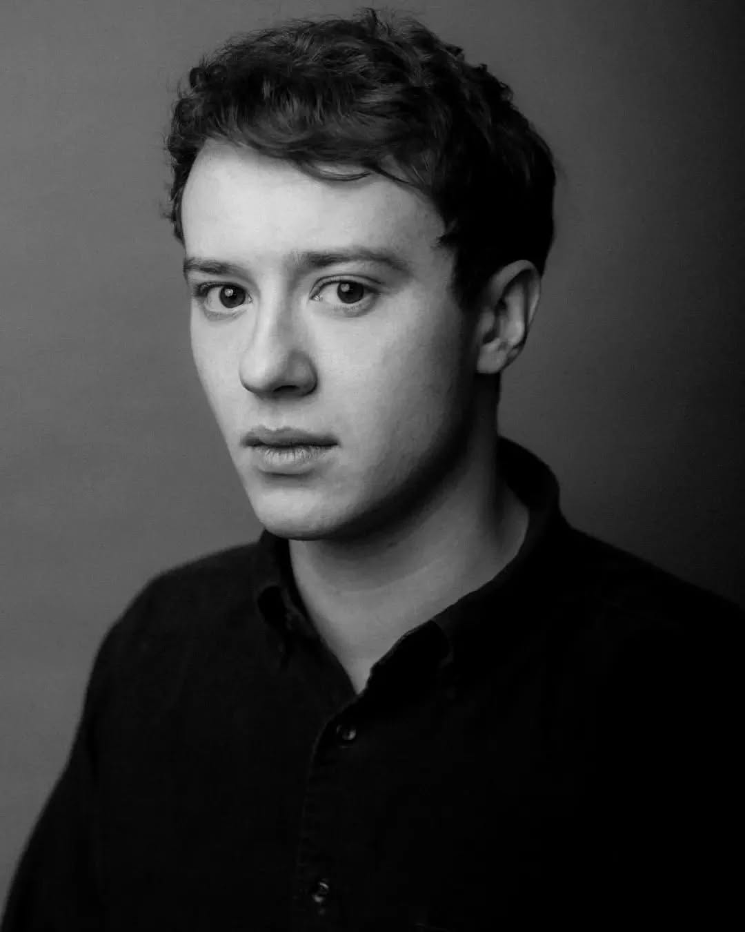 A black and white headshot of Joseph Quinn looking directly at the camera.