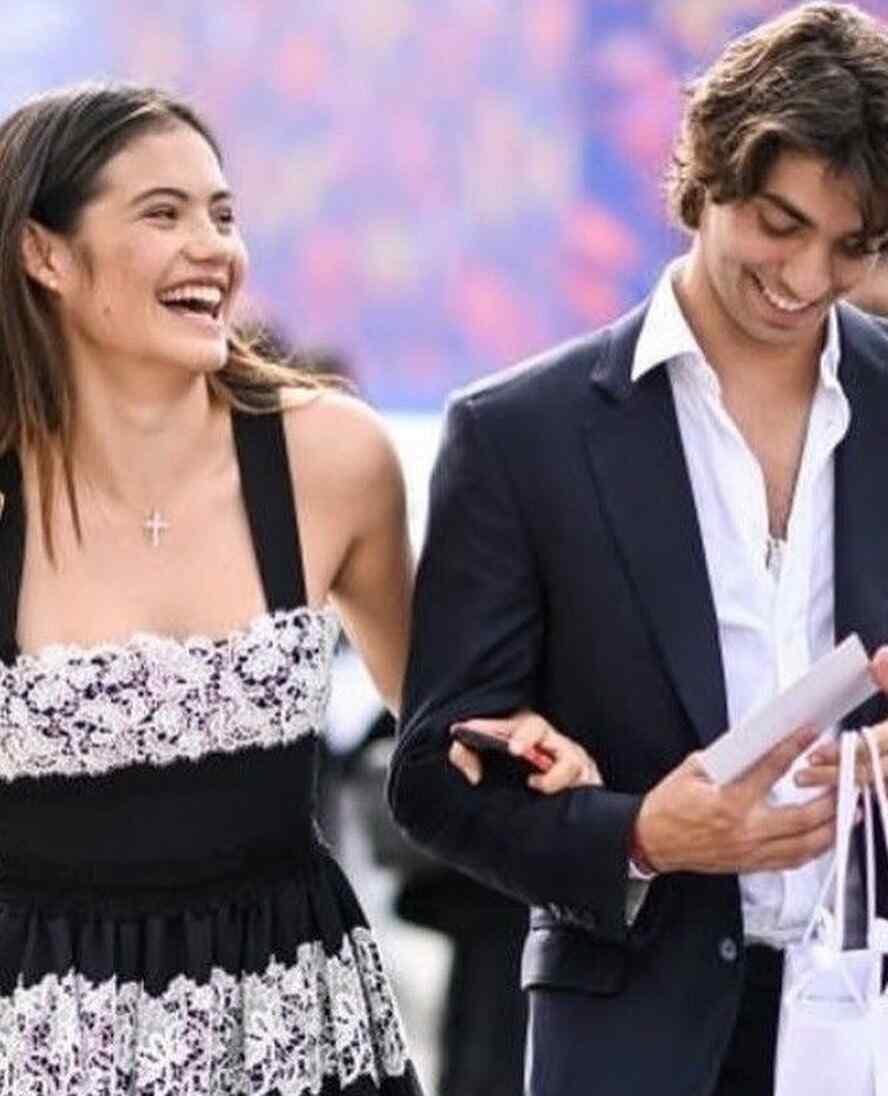 Emma Raducanu, smiling broadly, walks arm-in-arm with Carlo Agostinelli.