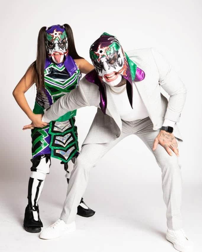 Penta El Zero Miedo, is in a gray suit over a white shirt, while his daughter is in a purple and green outfit.