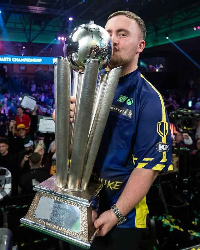 Luke Littler is kissing his World Darts Championship trophy.