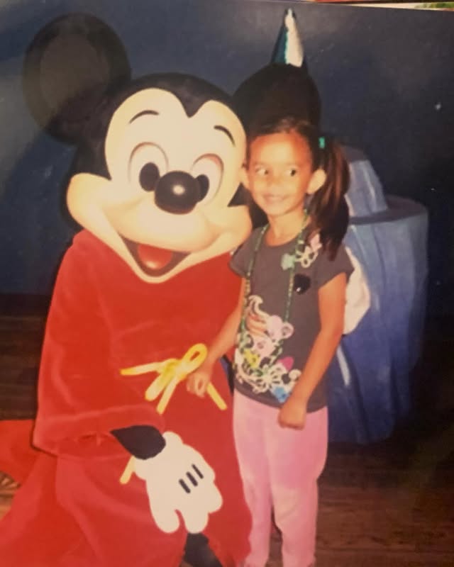 Sophia Hammons as a young girl, posing with Mickey Mouse in a red robe.