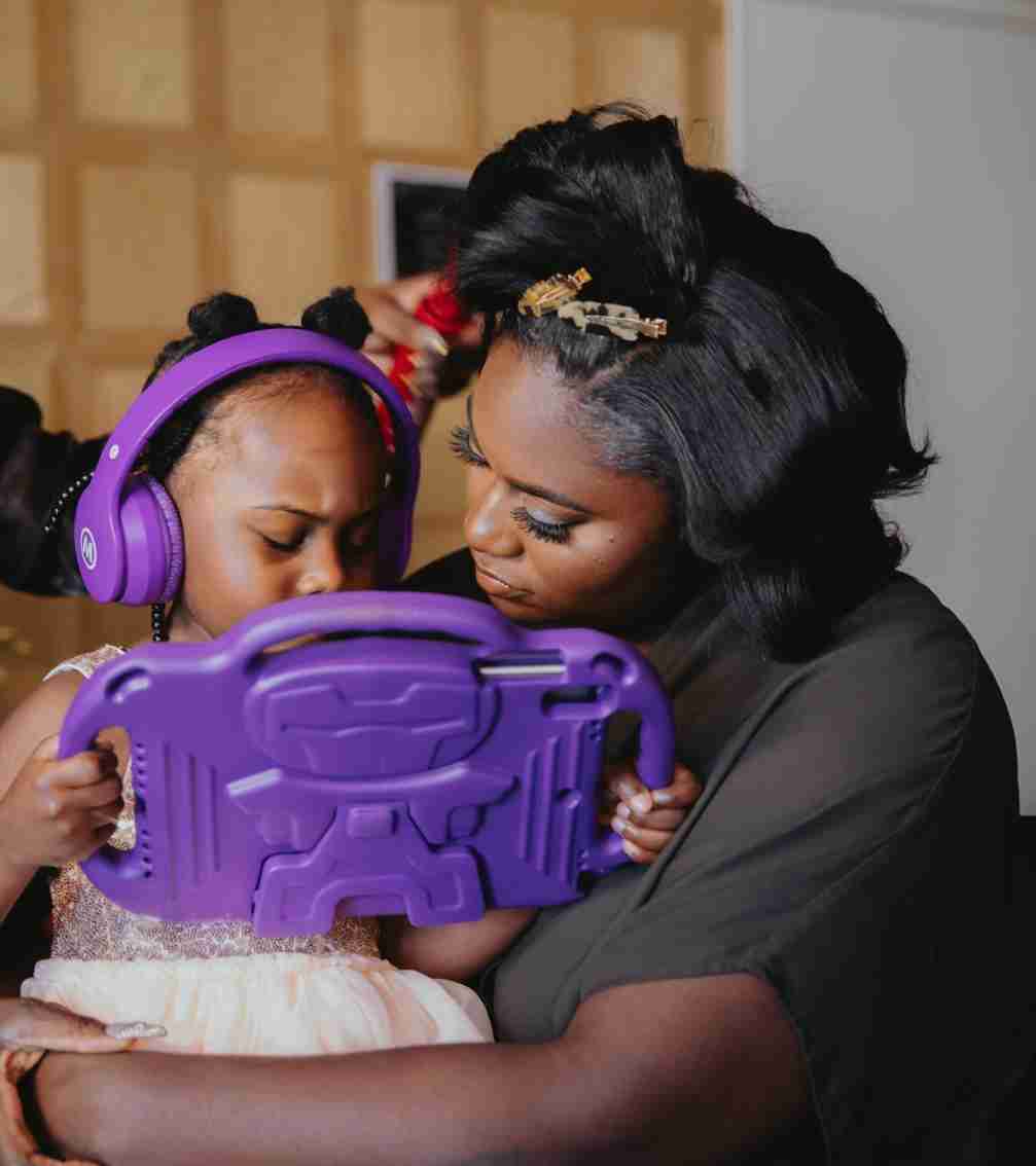 A heartwarming portrait of actress Danielle Brooks holding her young daughter, Freeya  who is focused on a tablet with purple headphones on.
