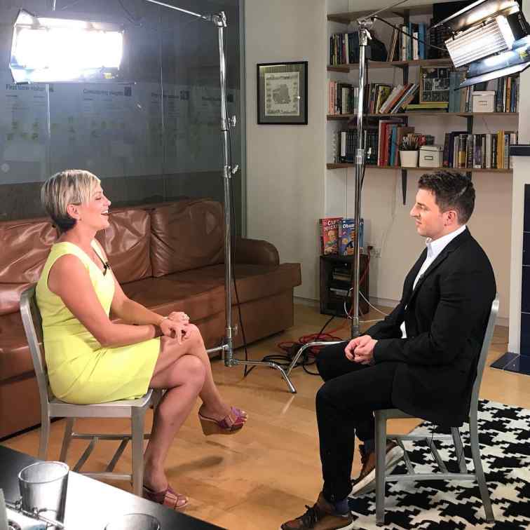 A behind-the-scenes shot of Brian Chesky, co-founder of Airbnb, being interviewed in a studio setting by Jamie Yuccas.