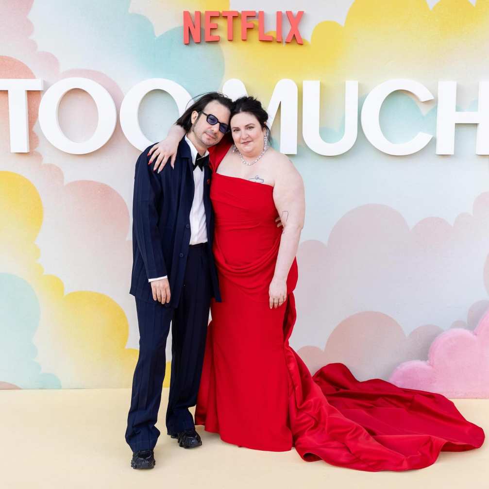Lena Dunham in a red gown with her arm around her husband, Luis Felber, who is wearing a navy suit, at a Netflix event.