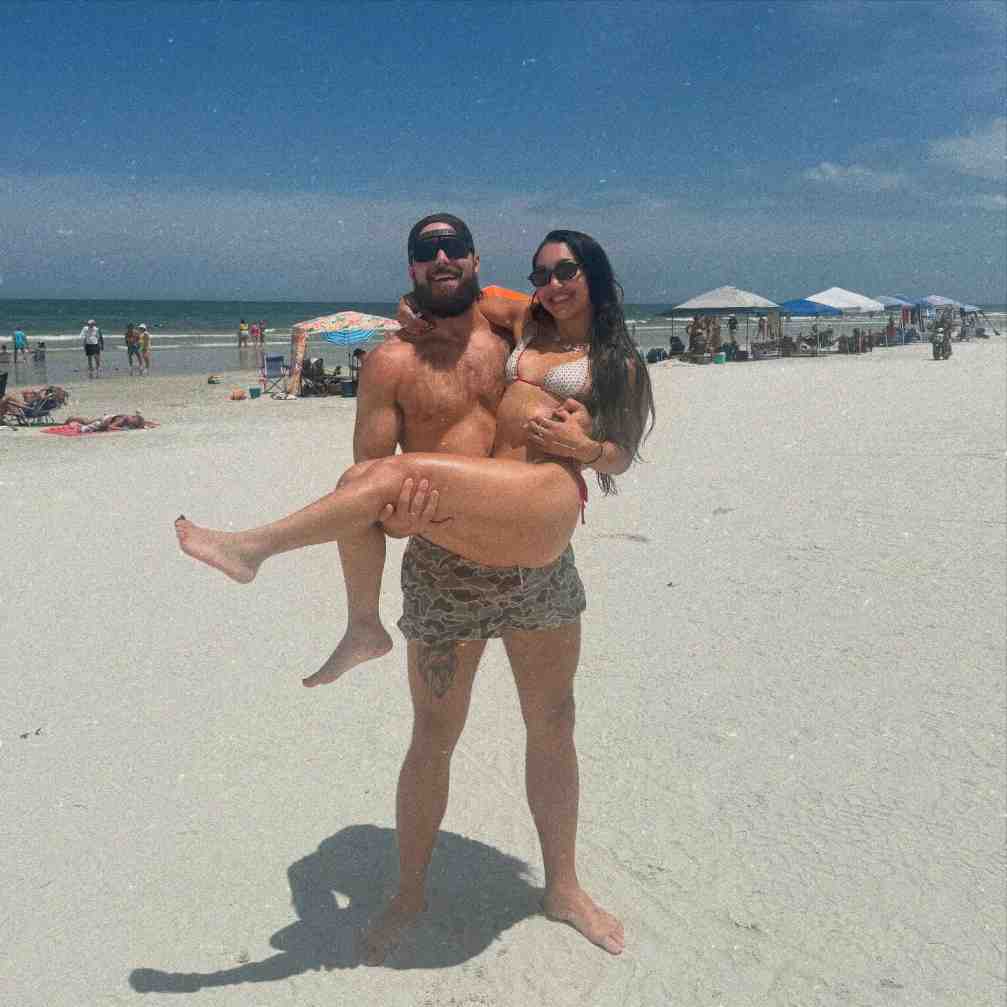 Drake Morreaux holding Roxanne Perez in his arms on a sunny beach.