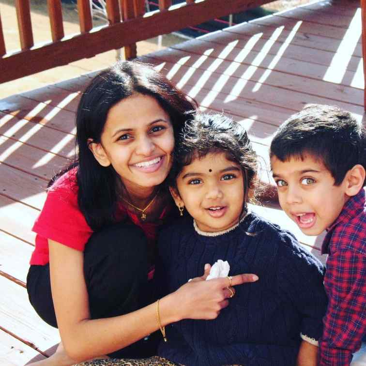 A young Avantika Vandanapu, in the middle, smiles with two other children on a wooden deck.
