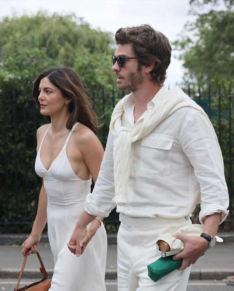 A photo shows actress Monica Barbaro and actor Andrew Garfield walking together, holding hands.