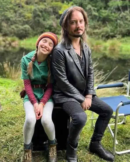 Actors Nell Fisher and Elijah Wood , sitting outdoors by a body of water.