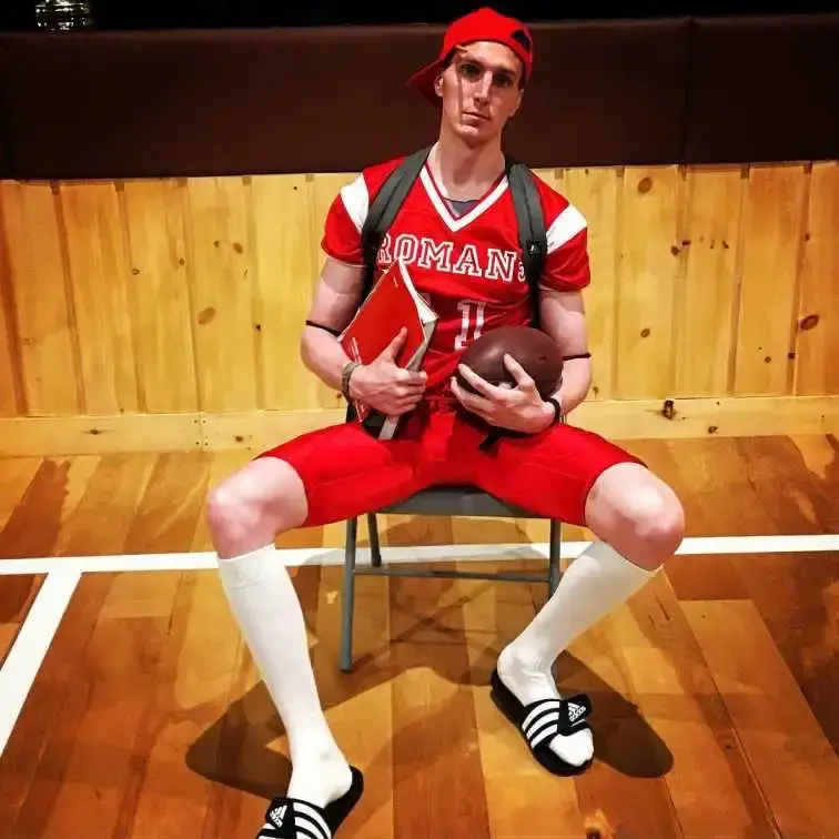 Alex Breaux, in a red football uniform, holding a football and a book.