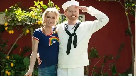 Julie Bowen and Jesse Tyler Ferguson from the television show Modern Family. Bowen, with her hair in pigtails, wears a t-shirt with a rainbow, and Ferguson, with his hand saluting, is in a sailor costume.
