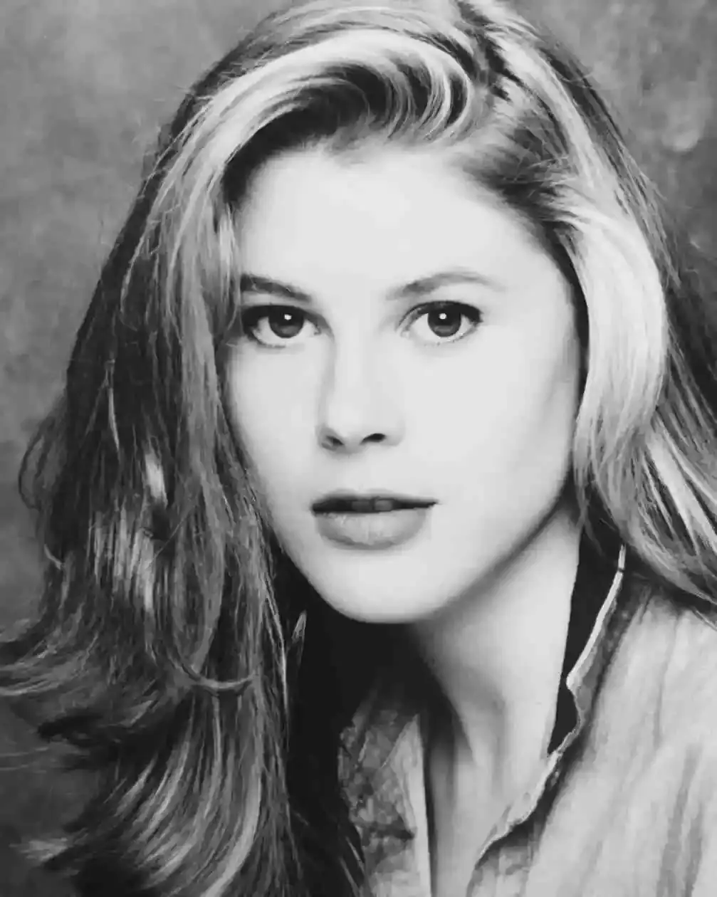 A black and white headshot of Julie Bowen in her younger years where she has long, wavy hair with lighter highlights framing her face and is looking directly at the camera.
