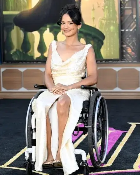 Marissa Bode, in a cream-colored sequin gown with a slit, sits in a wheelchair and smiles for the camera.