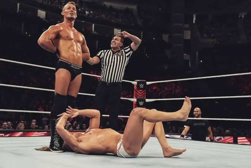 Professional wrestler Ludwig Kaiser stands over a downed opponent in a wrestling ring as the referee raises his hand.