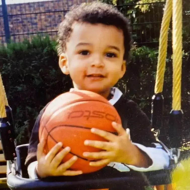 A young Victor Wembanyama, as a child, sits on a swing while holding a basketball.