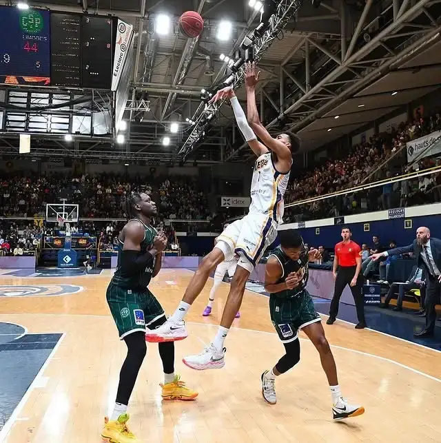 Victor Wembanyama, wearing a white jersey, jumps to shoot a basketball over two opponents.