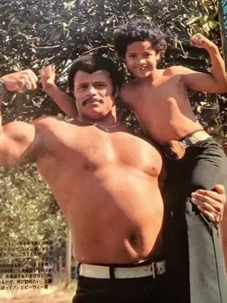 An adorable old photograph showing a young Dwayne "The Rock" Johnson posing with his wrestler father, Rocky Johnson.