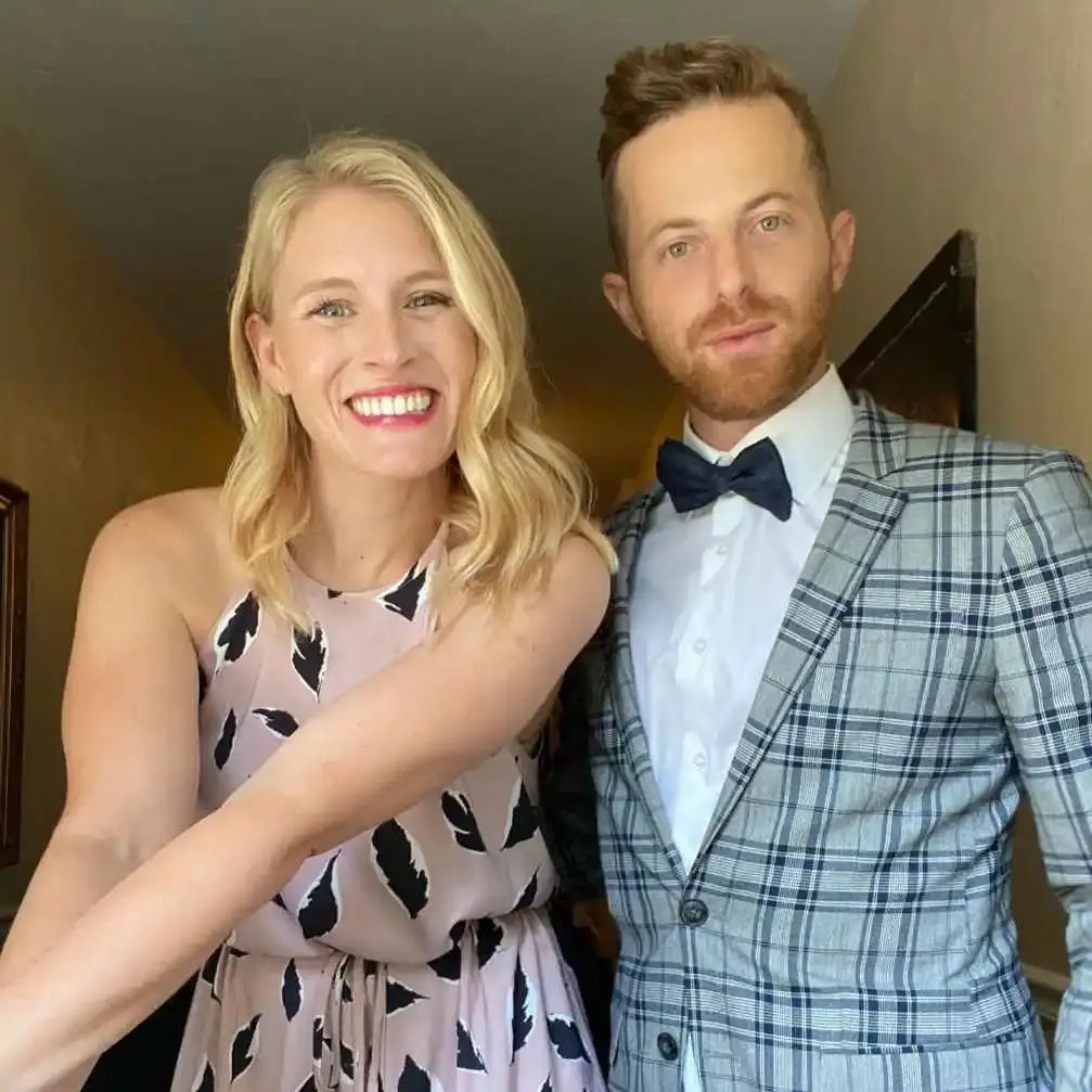 Ned Fulmer, in a plaid suit, and Ariel Fulmer in a pink dress are smiling while posing for a picture.