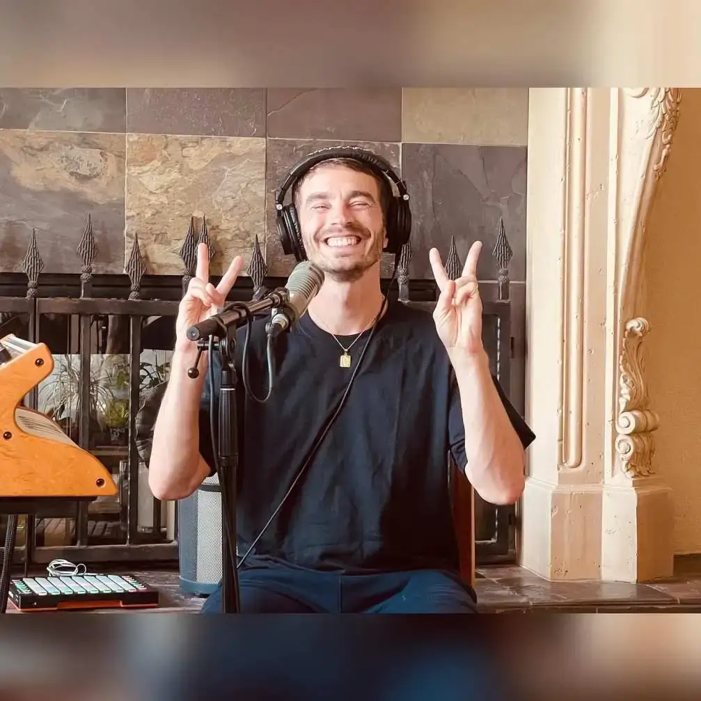 David Boyd, wearing headphones and a black t-shirt, gives a peace sign with both hands while sitting at a podcast microphone.