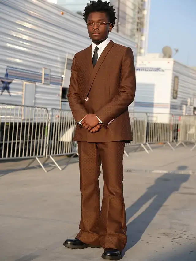 Miles Caton, standing outdoors in a brown suit with wide-legged pants and a black tie.