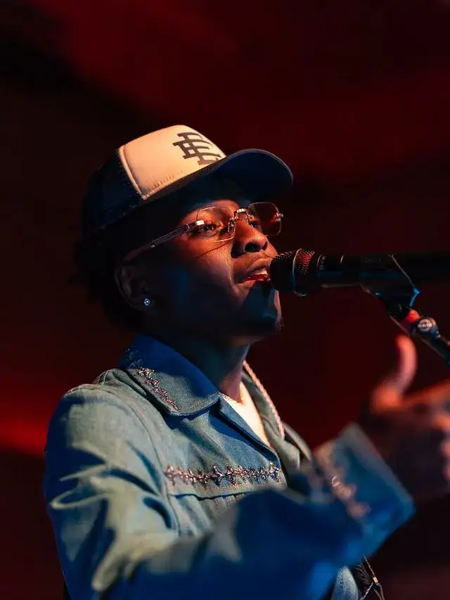 Miles Caton, wearing a trucker hat and a denim jacket, sings into a microphone on a stage.