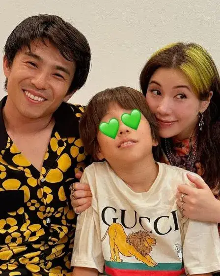 Riisa Naka, her husband Akiyoshi Nakao, and their son, whose eyes are covered by green heart emojis, all smiling at the camera.