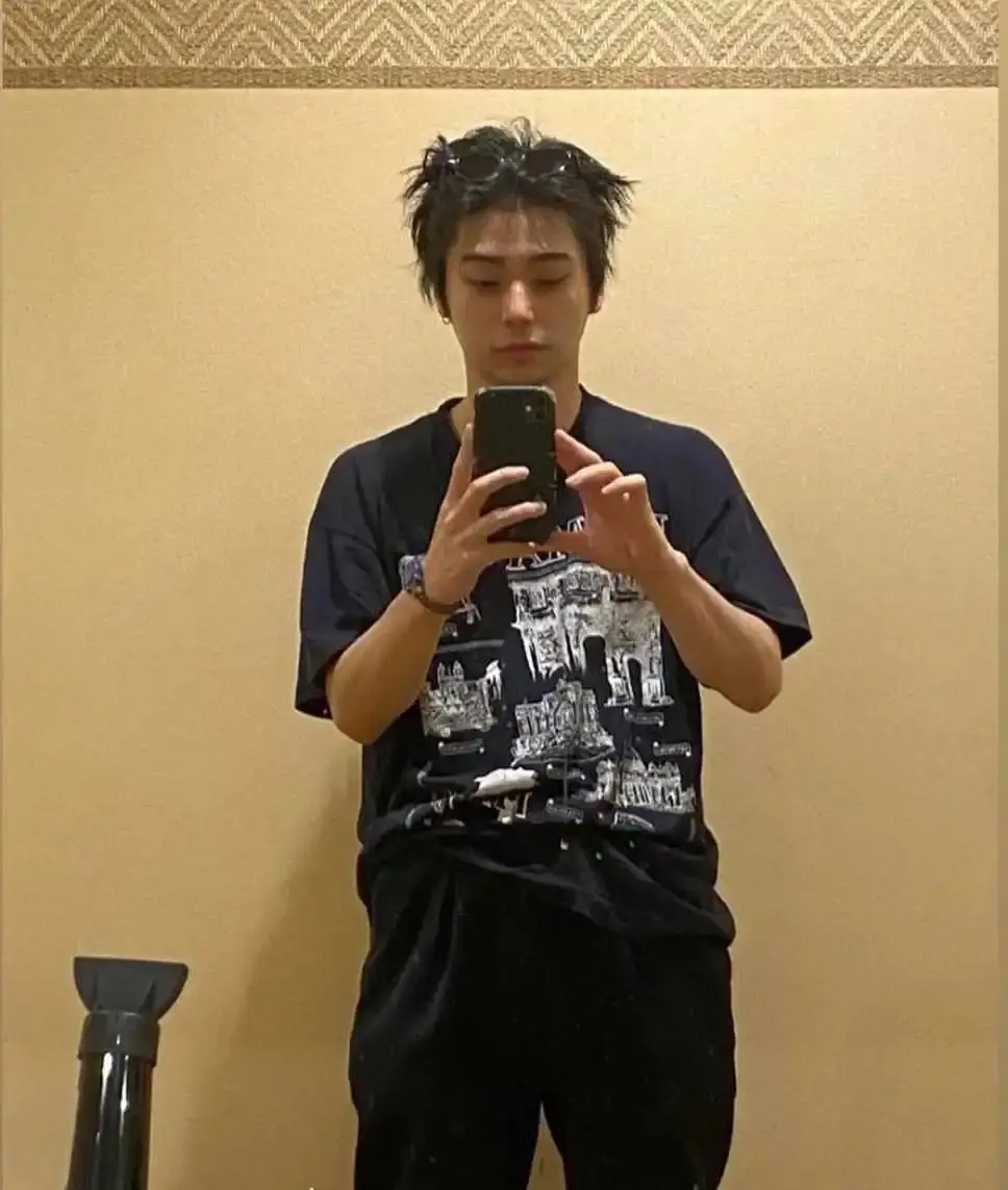 Nijirô Murakami taking a mirror selfie in a dark t-shirt with a graphic print, with his messy hair and sunglasses pushed up.