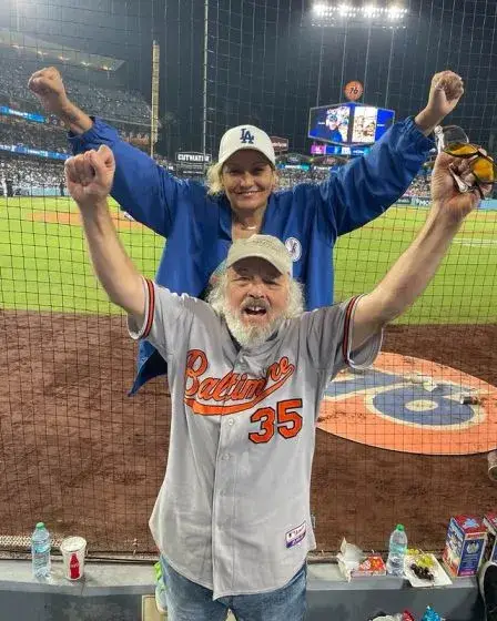 Actor Clint Howard and his wife Kat C. Cruz cheering at a baseball game, both with their fists raised in excitement.