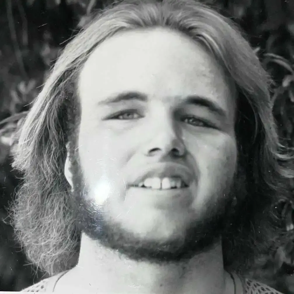 Black and white headshot of a young Clint Howard with long hair and a full beard, looking directly at the camera.