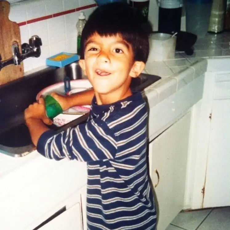 Young Eduardo Franco is standing by a kitchen sink and smiling with a playful expression.