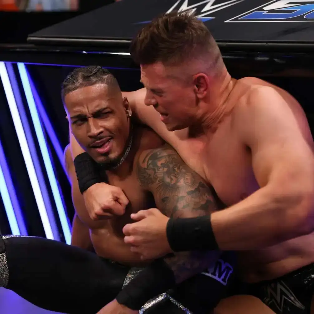 Professional wrestler Carmelo Hayes caught in a headlock by The Miz during a match in a wrestling ring.
