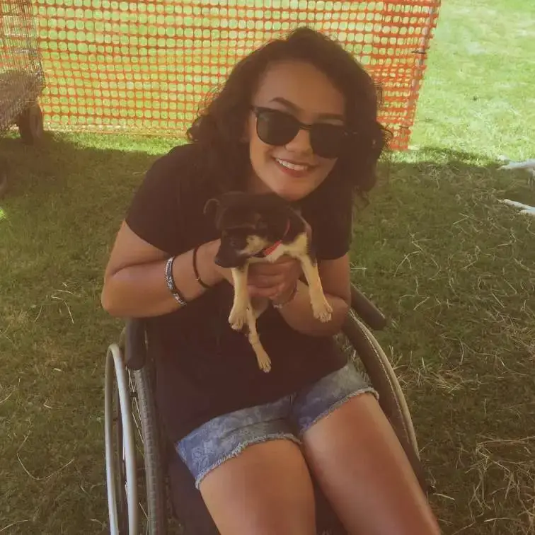 Marissa Bode smiles while sitting in a wheelchair, holding a small puppy with black and tan markings.