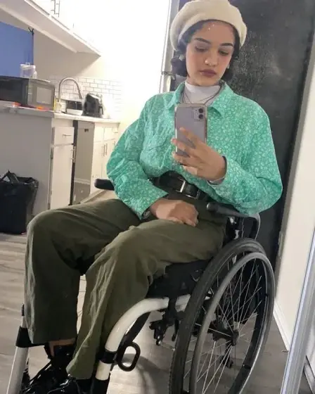 Marissa Bode sits in her wheelchair, taking a mirror selfie while wearing a white beret and a green patterned shirt.