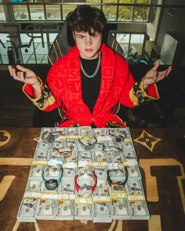 Jack Doherty sitting in a gaming chair, wearing a red velvet robe and diamond chain, posing with stacks of 0 bills and expensive luxury watches.