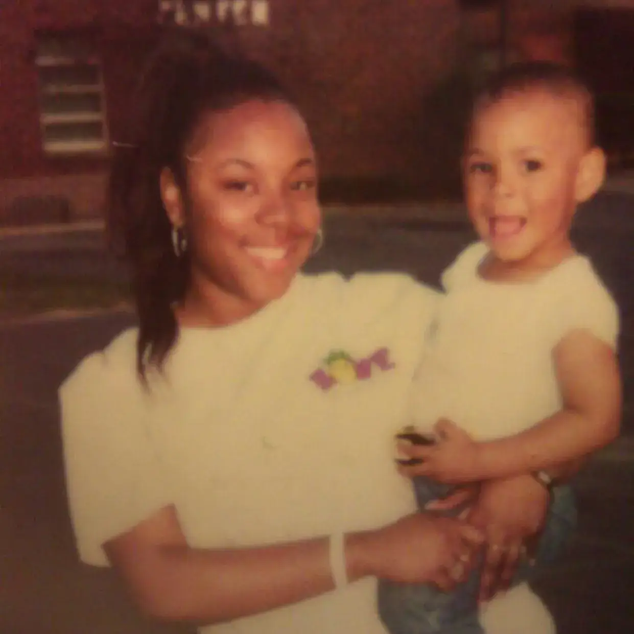 A vintage-style photo showing a young Black woman, Jahmyr Gibbs’ aunt, with her hair in a high ponytail, smiling warmly while holding a toddler in her arms.