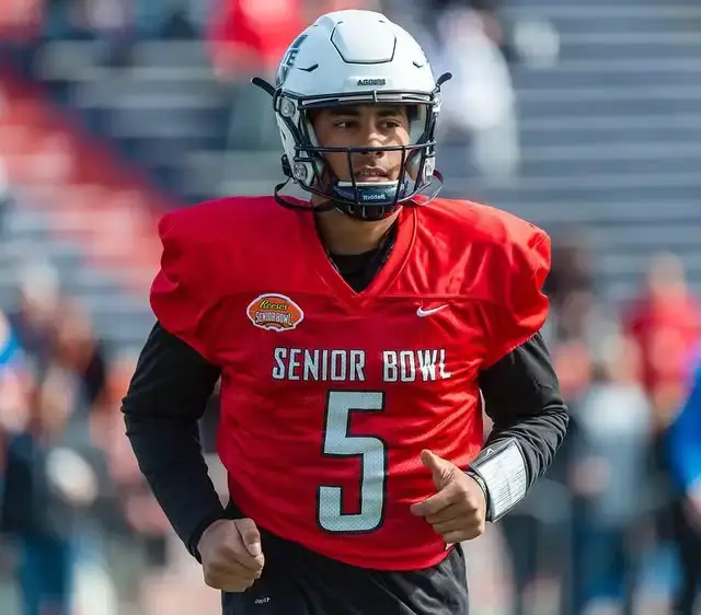 Quarterback Jordan Love, wearing a white helmet and a red Senior Bowl practice jersey with the number 5, runs on the field.