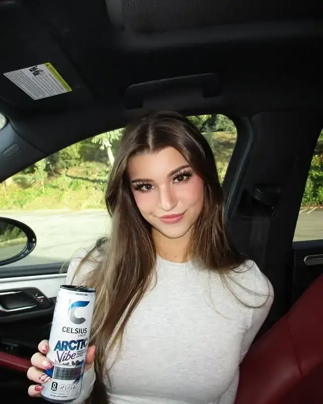 Brooke Monk sitting in a car, holding a can of Celsius Arctic Vibe energy drink and smiling at the camera.