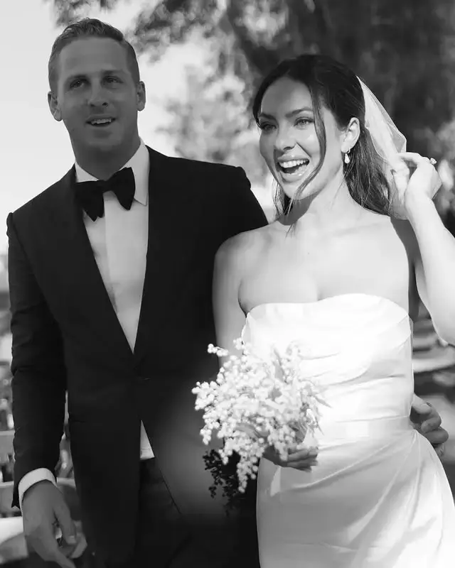 Black and white photograph of NFL quarterback Jared Goff in a tuxedo next to his wife, model Christen Harper, wearing a strapless wedding dress and holding a small bouquet.