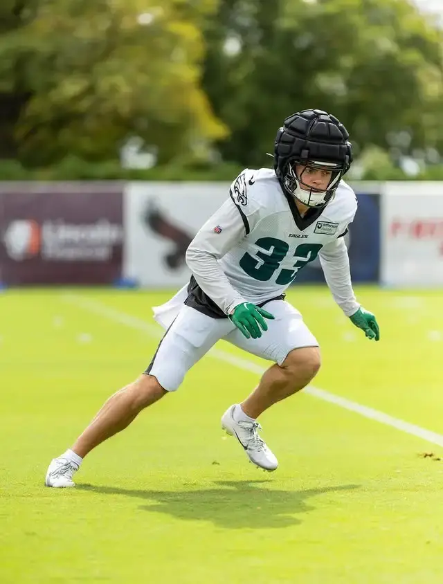 NFL player Cooper DeJean, wearing a Philadelphia Eagles practice jersey with the number 33 and a Guardian Cap over his helmet, runs during an outdoor training session.