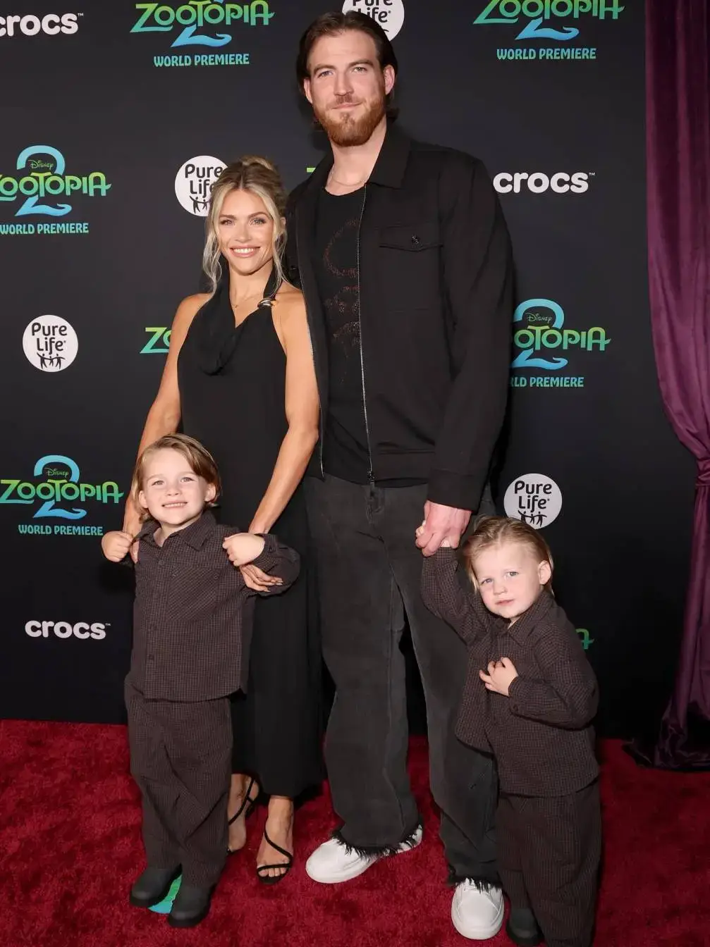 Witney Carson, her husband Carson McAllister, and their two young sons, Kevin and Jet, posing on a red carpet at the Zootopia 2 premiere.