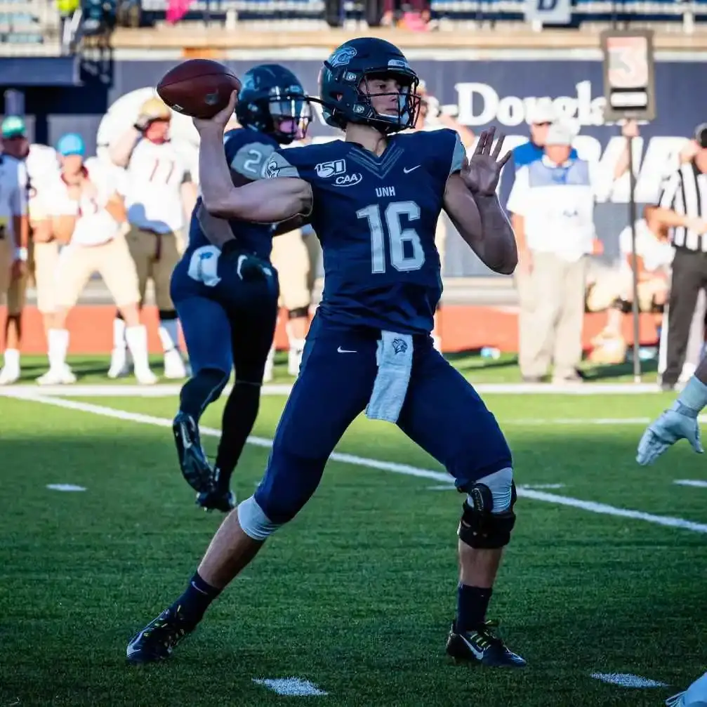 Football player Max Brosmer wearing a navy blue New Hampshire Wildcats uniform with the number 16, preparing to throw a football during a game.