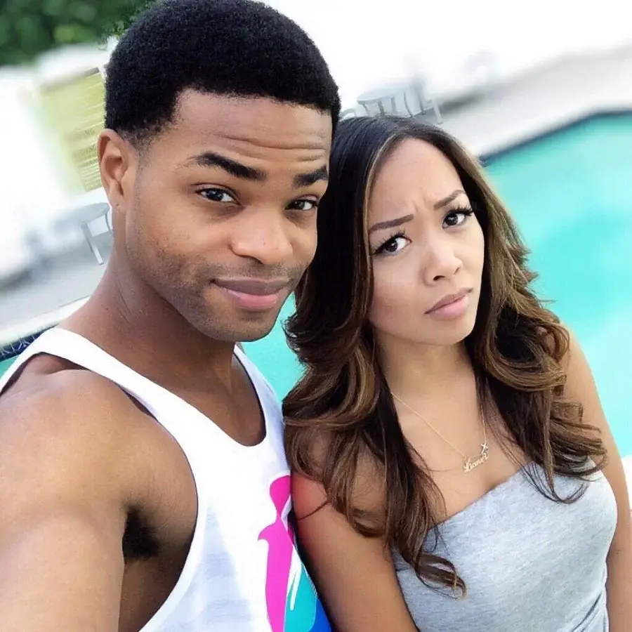 : King Bach and his girlfriend JaNina are sitting close together by a swimming pool, both looking directly at the camera in a selfie.