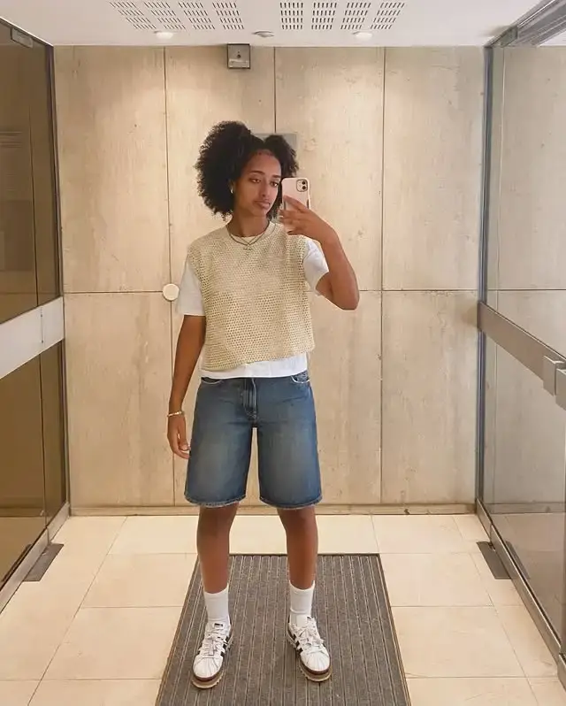 Full-length mirror selfie of soccer player Lily Yohannes wearing a casual outfit with baggy denim shorts and a knit vest over a white t-shirt.