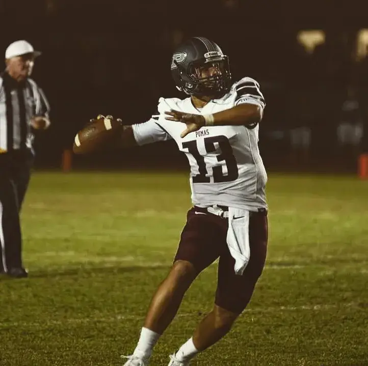 Football player Brock Purdy wearing a white jersey with the number 13 and a dark helmet, winding up to throw a football on a field at night.