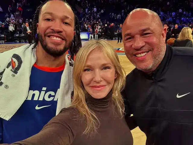 Actress Kelli Giddish smiles for a selfie with New York Knicks guard Jalen Brunson and his father, Rick Brunson, at a basketball game.