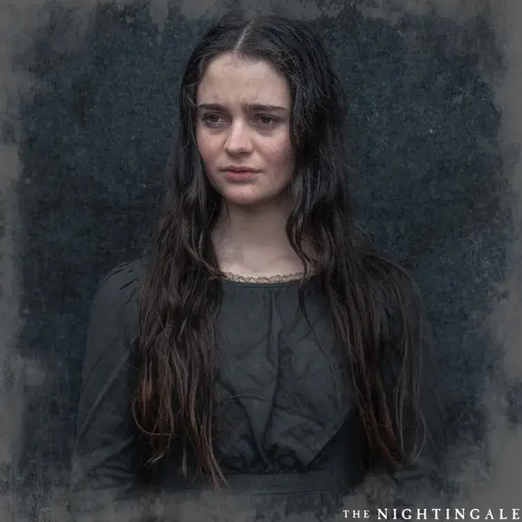 Actress Aisling Franciosi looks somberly to the side with long, wavy hair and a dark period-style dress in a still from the film The Nightingale.