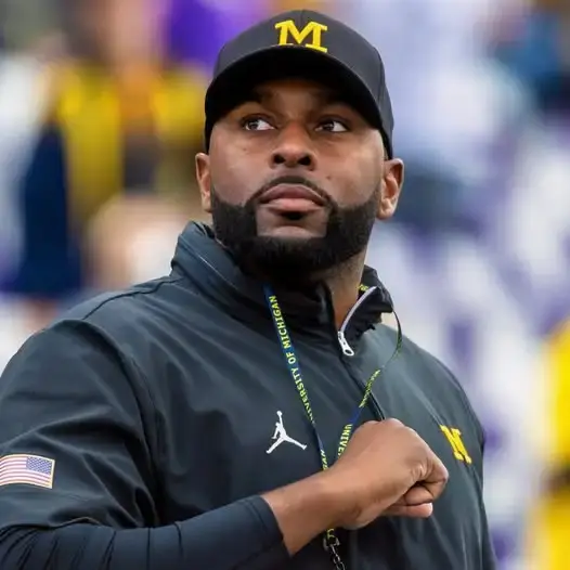 Former Michigan head coach Sherrone Moore speaks at a media day press conference while wearing a navy blue Michigan pullover.
