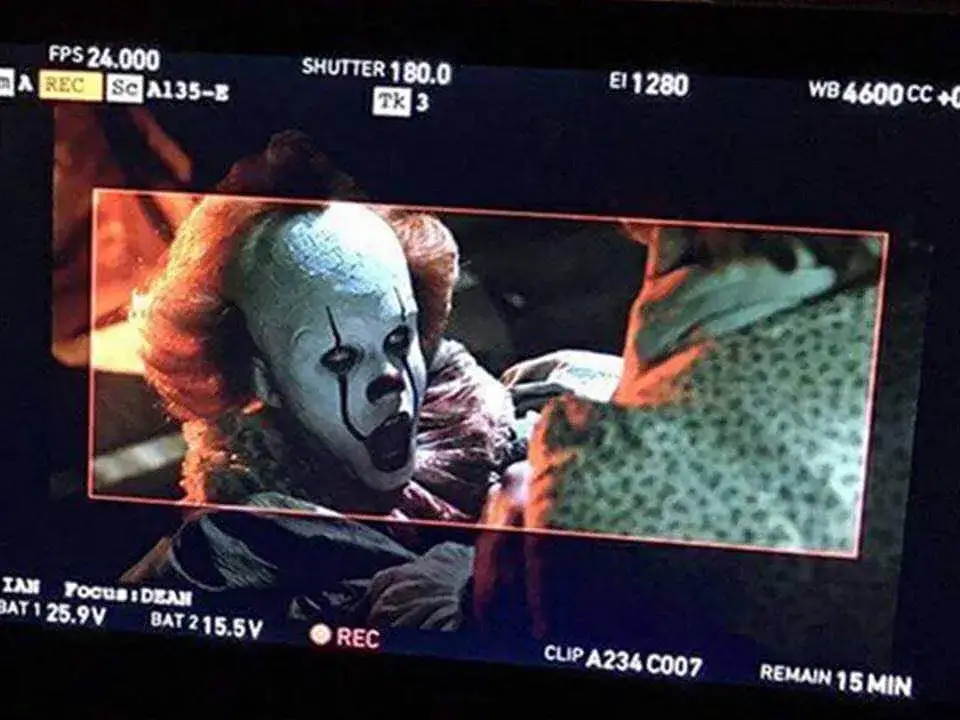 A camera monitor captures a haunting close-up of Bill Skarsgård as Pennywise the Dancing Clown, featuring his signature white face paint, red facial streaks, and a vintage-style ruffled collar.