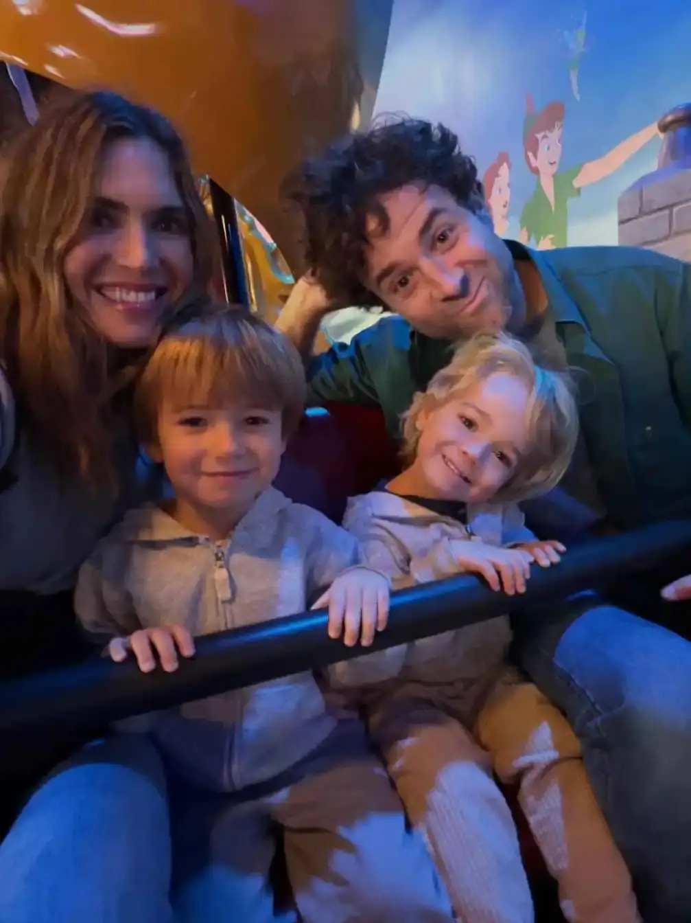 Mandy Moore and her husband Taylor Goldsmith smile with their two young sons while sitting together on an amusement park ride.