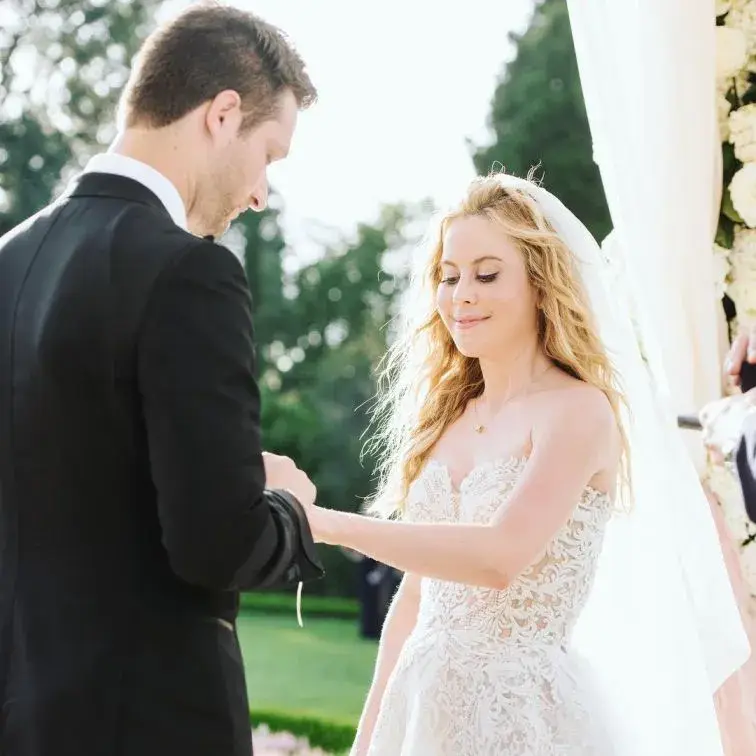 Tara Lipinski and her husband, Todd Kapostasy, smile joyfully while standing under a massive, 12-foot floral altar composed of 12,000 white roses and hydrangeas at their wedding in Charleston.